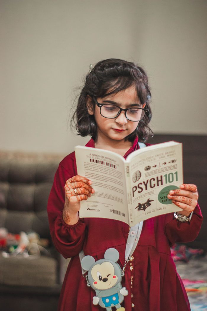 The Art of Drawing Readers In: Your attractive post title goes here A young girl with eyeglasses and henna tattoos reading a book indoors.